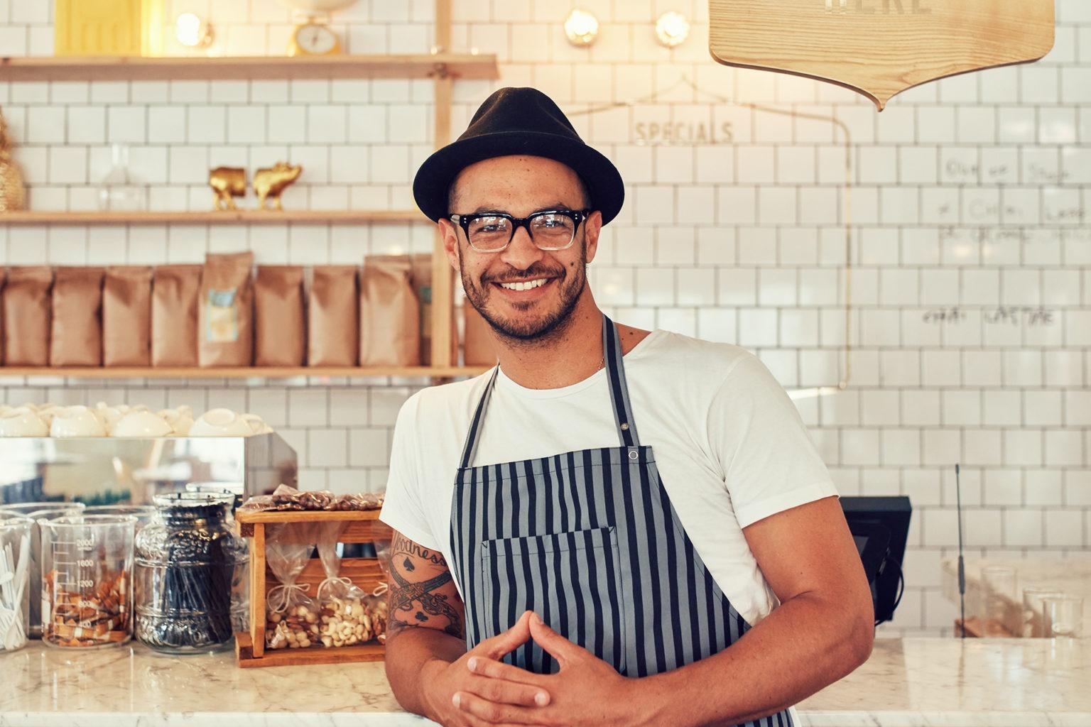 Dono de um pequeno negócio sorridente ao balcão do seu café