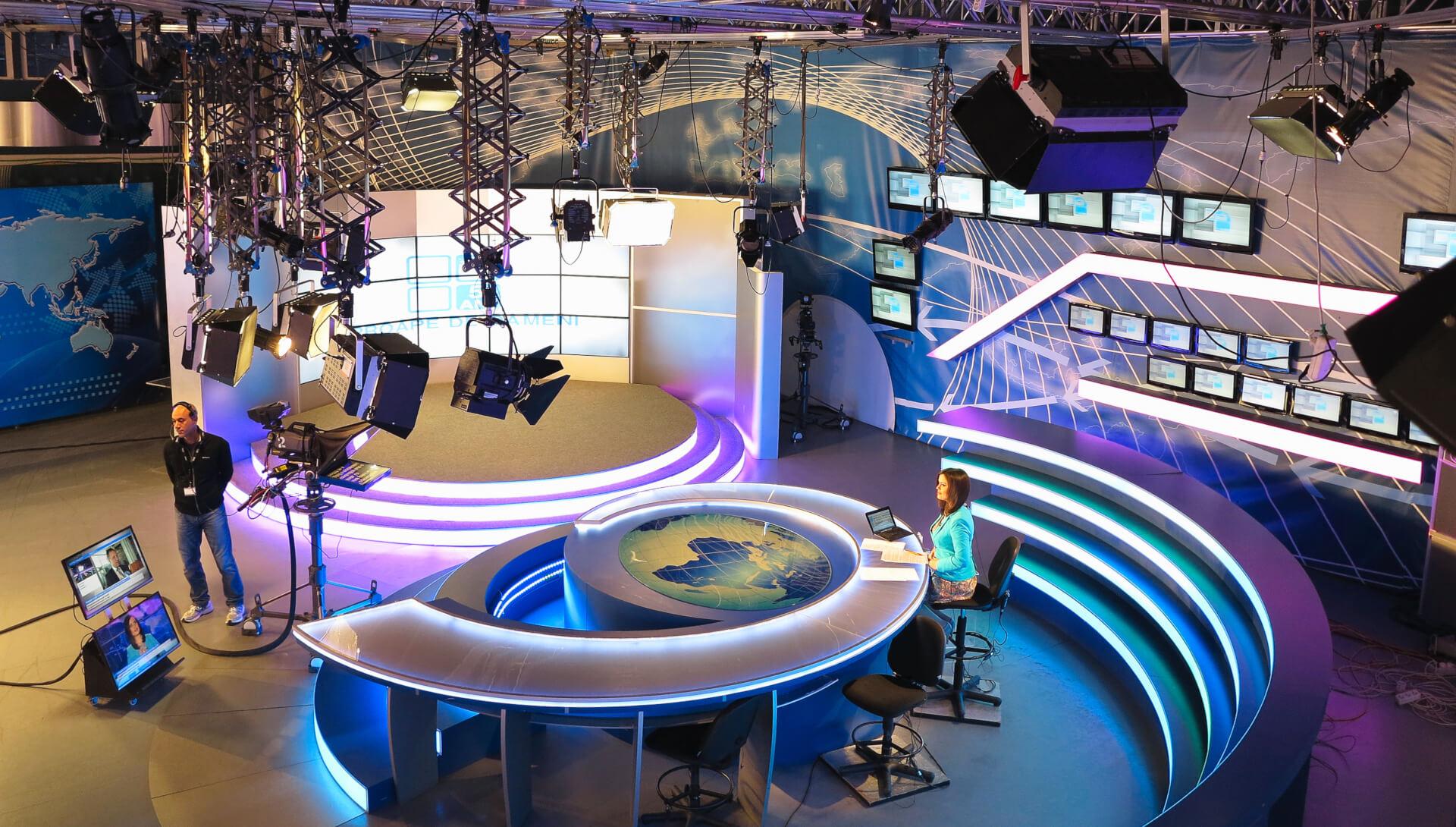 Estúdio de televisão com cenário iluminado, câmeras e apresentadores