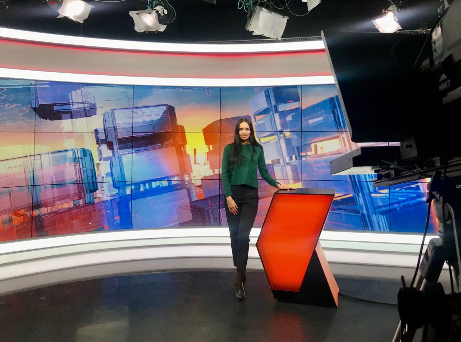 Apresentadora em estúdio de televisão com telão e câmeras