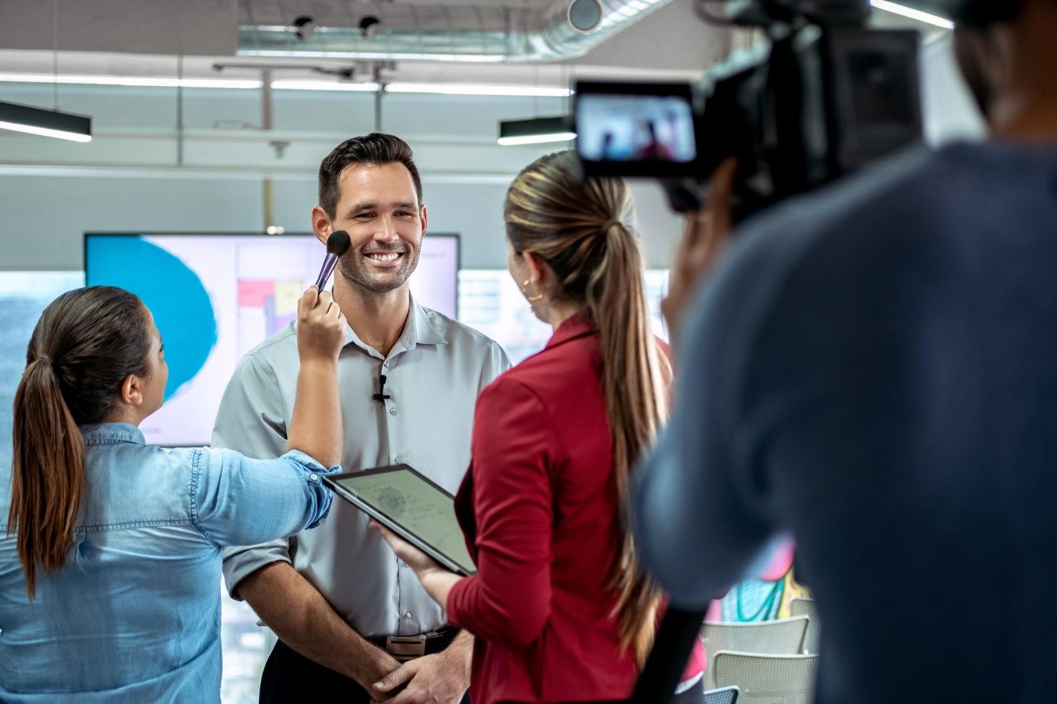 Corporate interview being filmed, with a camera operator, makeup artist and journalist